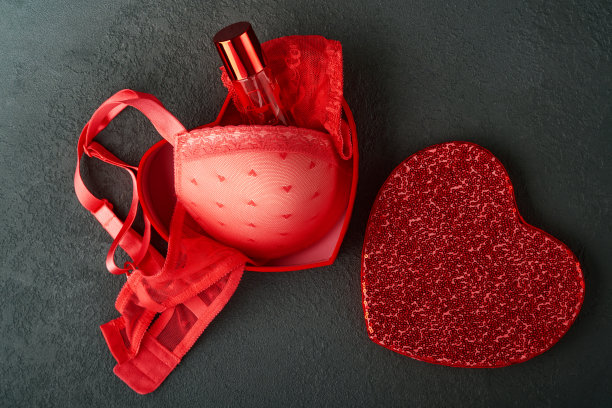 红色性感内衣和内裤在盒子上的黑色背景。女人性感内衣套装与玫瑰和香水。妇女节或情人节的礼物创意与复制空间。不论是对男人还是对他来说都是惊喜。俯视图图片下载