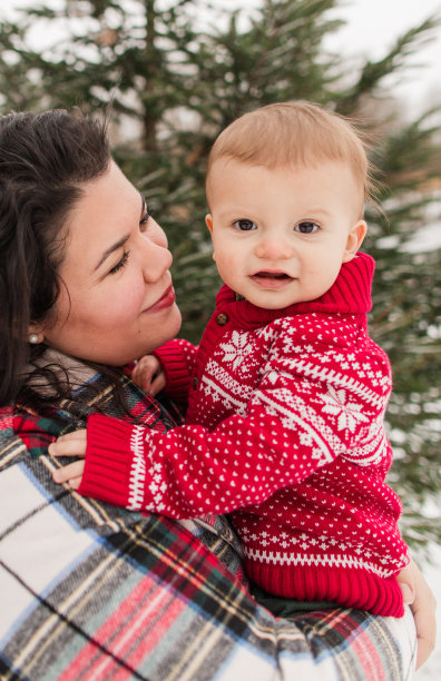 12个月大的男婴穿着红色和白色针织圣诞毛衣依偎在母亲的怀里图片下载