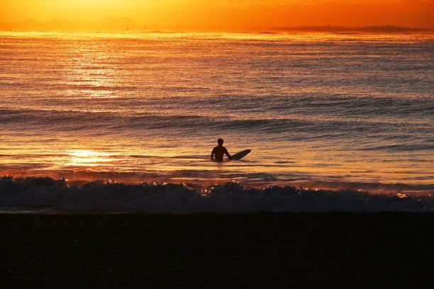 冬天黎明时分海滩上的冲浪者。图片下载