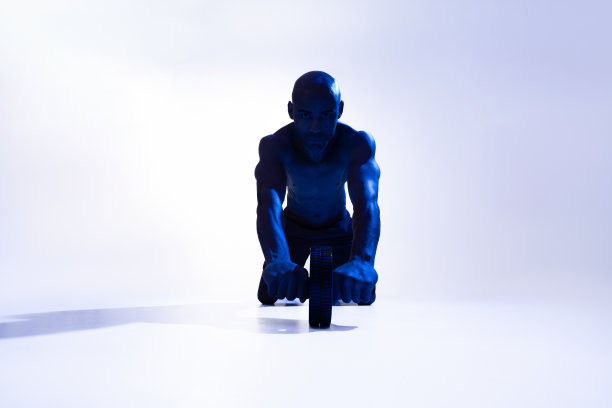 健美运动员工作在他的腹肌与腹肌辊在工作室的背景与彩色滤镜图片下载