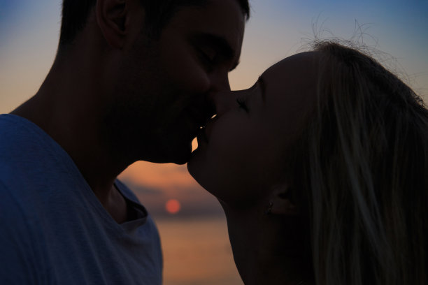 一对年轻夫妇的剪影，以海上日落或日出为背景。图片下载