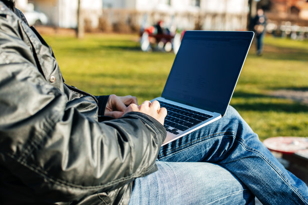 一个男人坐在长凳上，在街上用笔记本电脑工作，他的手特写。远程工作概念图片下载