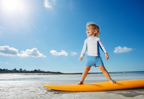 美丽的卷发女孩站在冲浪板学习在海滩图片下载