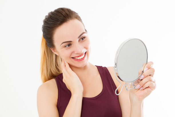 年轻的白人妇女在镜子里看着脸上的皱纹孤立在白色背景上。护肤和化妆概念。本空间图片下载