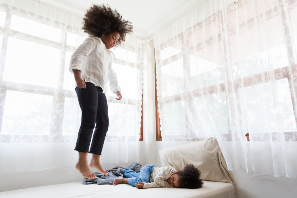 两个非洲裔美国小女孩在家里的床上玩耍跳跃。孩子，游戏和假期的概念图片下载