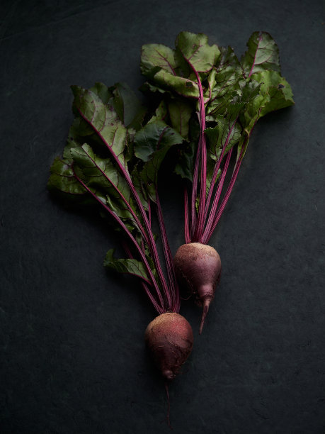 新鲜有机甜菜，两个完整的甜菜根，带球茎和叶子，隔离在深色背景上图片下载