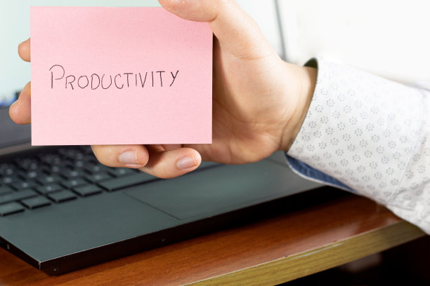 在办公室的电脑前，一个男人的手展示了一张写着“生产力”的便利贴图片下载