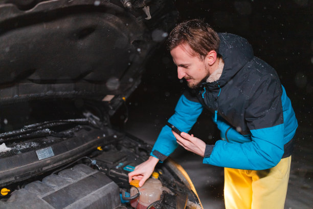 在下雪的夜晚，一个年轻人在他的汽车引擎盖下张望图片下载