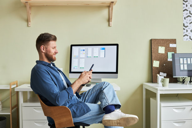 微笑的年轻人在工作场所放松，使用智能手机图片下载