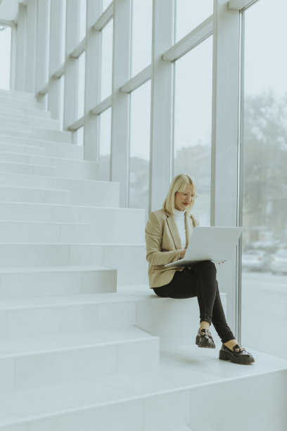 带着笔记本电脑的女商人站在现代化的办公室楼梯上图片下载