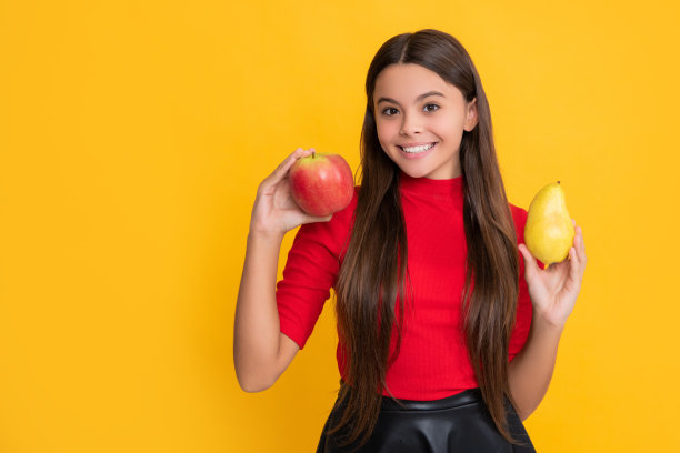 高兴的女孩拿着新鲜的苹果和梨在黄色的背景图片下载