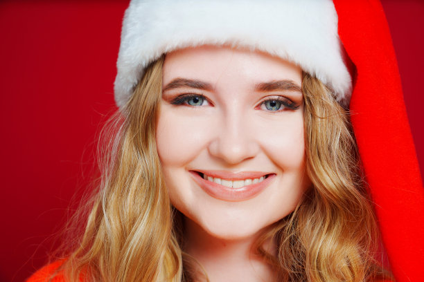 关闭了。一个红色背景上戴着圣诞老人帽子的美丽女人。图片下载