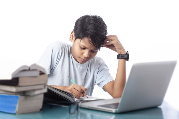 认真阅读和写作的学生在书桌上与电脑和书籍的考试图片下载