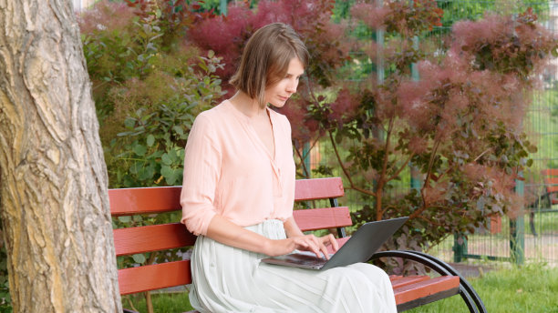 年轻女子坐在公园的长椅上，用笔记本电脑工作图片下载