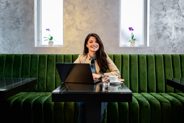 微笑的女人在咖啡馆使用笔记本电脑在线工作的肖像。图片下载