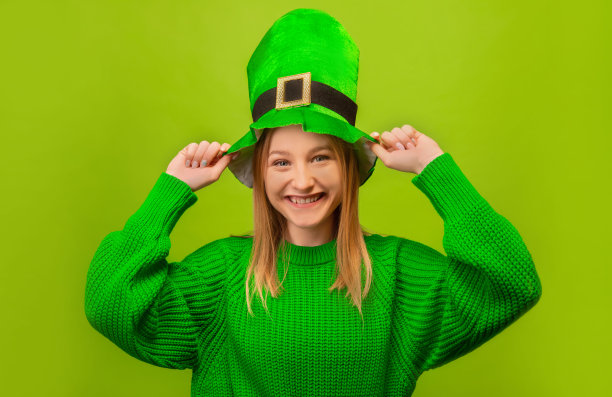 快乐的笑着微笑的女孩拿着绿色的小精灵帽子，穿着绿色的毛衣，看着相机孤立在彩色的绿色背景上。

圣帕特里克节庆祝概念。图片下载