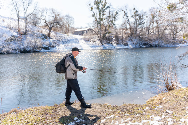 初春，一个渔夫背着背包，拿着鱼竿在白雪覆盖的河边捕鱼图片下载