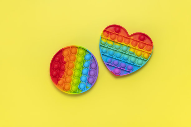 流行硅胶多色抗压力玩具pop在心形和圆形的黄色背景平铺顶视图。时髦的现代感官儿童玩具，烦躁推挤吧图片下载