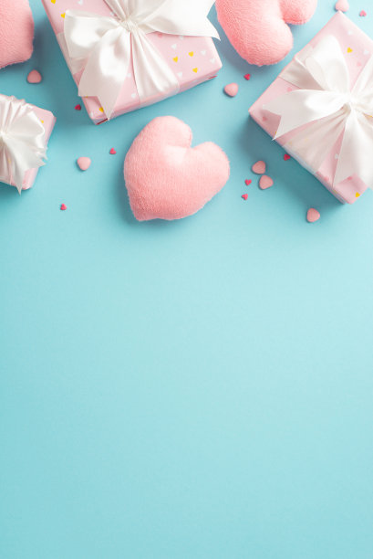 情人节的概念。俯视图垂直照片粉红色礼盒与白色缎带蝴蝶结心形软枕头和洒在孤立的浅蓝色背景与复制空间图片下载
