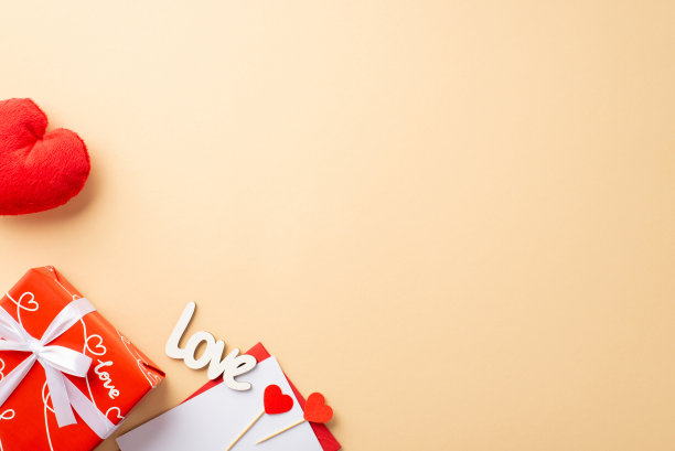 情人节的概念。顶部视图照片红色礼盒带蝴蝶结信封与信蓬松的心玩具和铭文爱在孤立的粉彩米色背景与空白图片下载