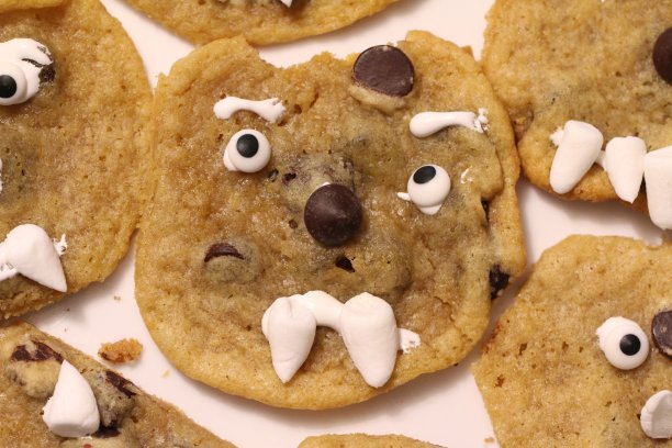 一组自制的，不完美的巧克力饼干，每个都有一张友好但不苟言笑的脸，用糖果和棉花糖做成。这款特色饼干有棉花糖般的尖牙和弯曲的眼睛。图片下载