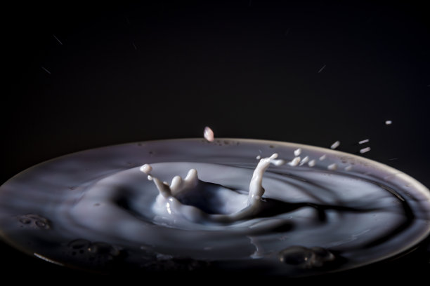 彩色鲜奶滴入另一种颜色的牛奶杯与深色背景图片下载