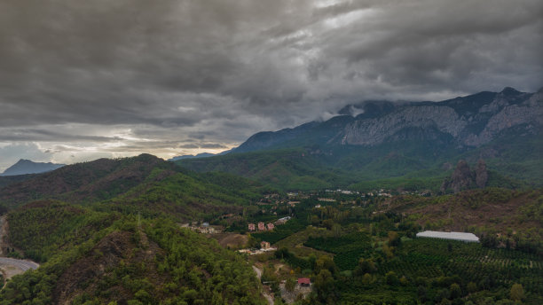 无人机航拍图。在山脚下的居民区上空飞行。绿色的树木。高速公路。灰色的云。高质量照片图片下载