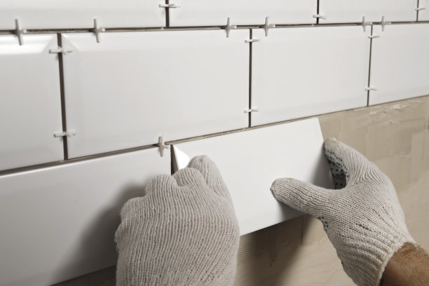 男工师傅在厨房墙上铺瓷砖。修理工放置白色现代瓷砖，涂抹粘合剂。建筑工人在维修改造工作中安装瓷砖。专业瓷砖，4K图片下载