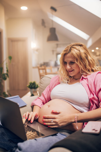 年轻的孕妇在家里用笔记本电脑工作图片下载