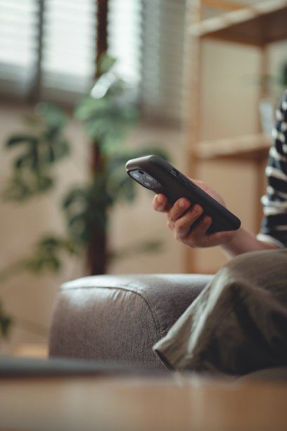 在家里客厅沙发上放松时，女性使用智能手机的手特写镜头。图片下载