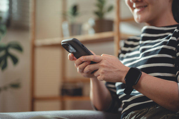 在家里客厅沙发上放松时，女性使用智能手机的手特写镜头。图片下载