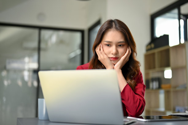 不开心和无聊的年轻亚洲女商人坐在她的办公桌上看着笔记本电脑屏幕图片下载