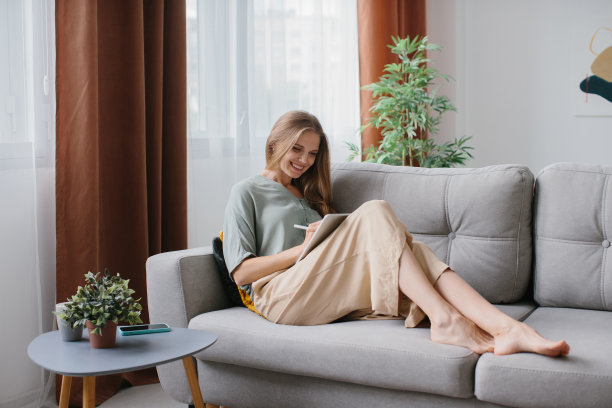 一个女孩坐在沙发上，手里拿着平板电脑和手写笔图片下载