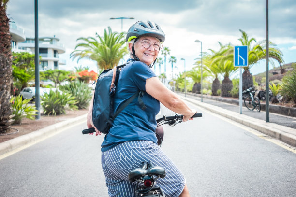 快乐有吸引力的退休妇女带着头盔和背包在城市街道上享受电动自行车的活动-可持续移动的概念图片下载