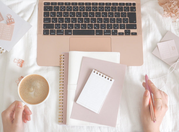 笔记本电脑和笔记本放在床上，女人的手拿着拿铁咖啡，电脑的形象柔和大气图片下载