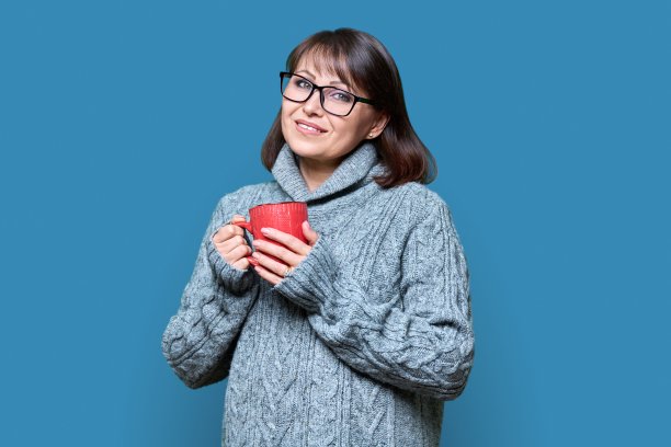 冬季肖像快乐的女人在毛衣与马克杯在蓝色的背景图片下载