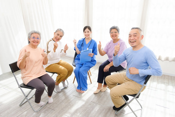 在老年群体治疗过程中，护理治疗师与一群竖起大拇指围成一个圈的亚洲老年人坐在一起，检查身心健康状况。养老院为图片下载