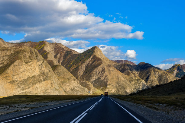 弯弯曲曲的柏油路穿行在高高的雪峰、黄色的沙漠、秋绿的森林和蓝天之间。高速公路上的汽车，背景是山上的风景图片下载