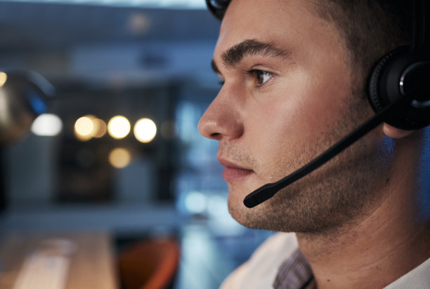 呼叫中心，晚上，办公室里拿着麦克风为客户服务、电话营销和销售提供咨询的人。在客户关系管理领域工作的男性，请联系我们和电信业务部门寻求支持和帮助图片下载