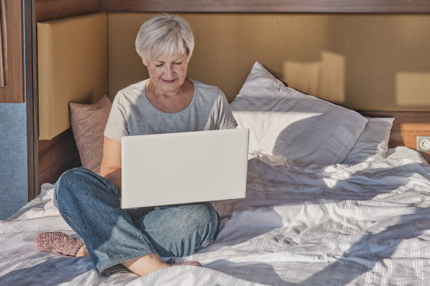 成熟的女人在床上使用笔记本电脑。图片下载