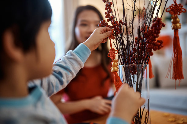 近距离的男孩挂在树枝上的中国新年装饰品和他的母亲装饰家。图片下载