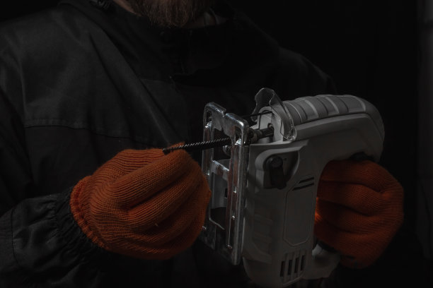 电动拼图，在妈妈的手锯木材隔离在黑色背景图片下载