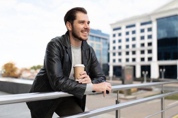 一个年轻人手里端着一杯咖啡站在外面，看着这座城市图片下载