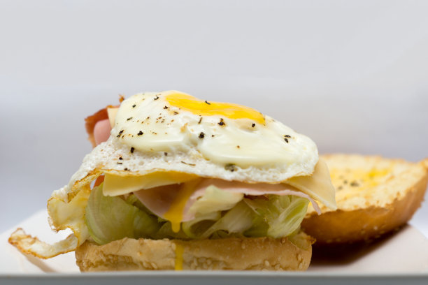 自制鸡蛋夹心面包配奶酪，火腿和培根。三明治配煎蛋和蔬菜。早餐的概念图片下载