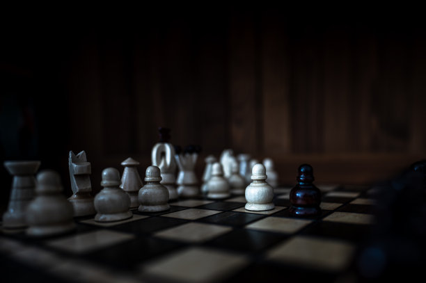 模糊的黑白背景与低深度的焦点。一套木制棋子元素站在棋盘上的黑暗背景。领导力，团队合作，伙伴关系，商业战略理念。图片下载