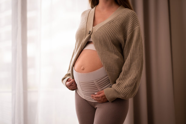 无法辨认的孕妇触摸婴儿隆起，腹部靠近窗户，裁剪的照片，柔和的颜色。自然、健康、美丽的怀孕理念。文本的Copyspace图片下载