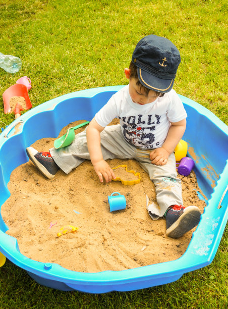 一个小男孩坐在花园里一个贝壳形状的沙坑里图片下载