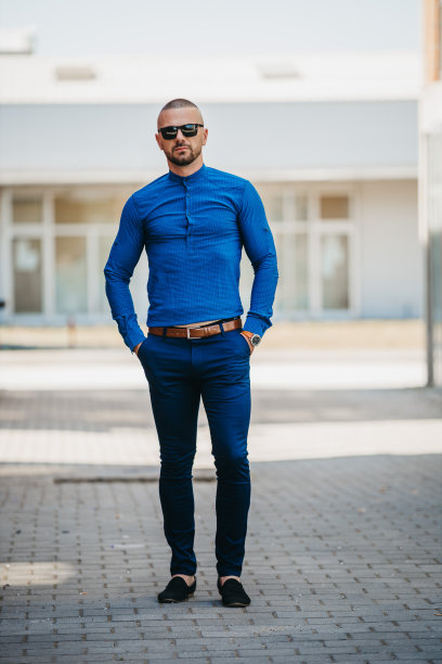 帅气的白人男子穿着优雅的蓝色衬衫，戴着太阳镜在户外摆姿势图片下载
