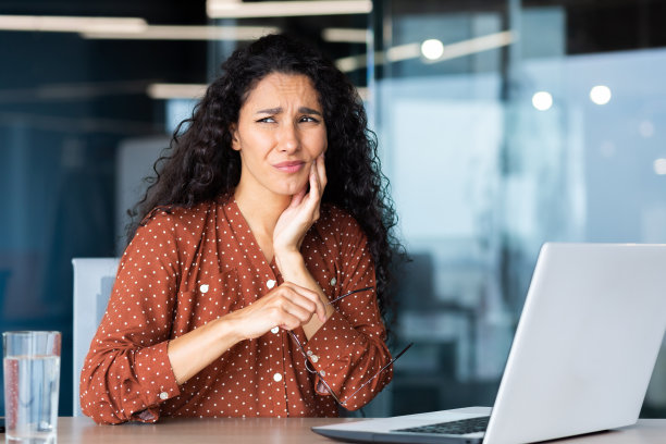 办公室职员工作中牙痛，使用笔记本电脑的拉丁美洲女商人图片下载