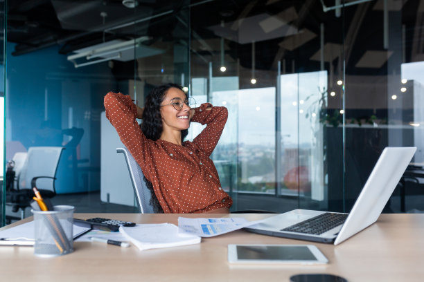 一位在办公室里笑着，双手放在脑后的年轻拉丁美洲女性图片下载